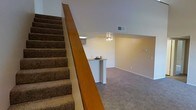 This two-floor residence offers a practical and well-organized layout designed for comfortable everyday living. A prominent carpeted staircase with a warm wood banister serves as a central architectural element, connecting both levels and adding a classic touch to the interior.

The lower level opens into a spacious living area finished with wall-to-wall carpet, creating a cozy and inviting atmosphere. A built-in breakfast bar with a laminate countertop provides a convenient space for casual dining or entertaining, serving as a natural divider between the living area and adjacent spaces. A ceiling fan with integrated lighting illuminates the area efficiently, while the vaulted ceiling above the staircase adds a sense of height and openness to the space.

The neutral wall tones throughout create a clean, versatile backdrop that accommodates a variety of interior design styles. HVAC vents are visibly integrated into the upper wall, ensuring year-round climate comfort. Clean baseboards and well-maintained finishes are evident throughout, reflecting the overall condition of the space.

Overall, this two-story residence combines functional design with comfortable finishes, making it a well-suited space for a range of living arrangements.