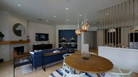 This thoughtfully designed single-floor space offers an open-plan layout that seamlessly integrates multiple functional zones into one cohesive environment. The lounge area anchors the space with a deep navy blue sofa, a sleek media console with a wall-mounted TV, and a striped area rug that adds a touch of casual sophistication. Adjacent to the lounge, a round wood dining table surrounded by light mint chairs provides an inviting spot for gathering, elegantly lit by a cluster of striking copper globe pendant lights that serve as a visual centerpiece. A built-in workstation area set against a rich navy blue accent wall offers dual computer stations, making it ideal for productivity within a shared setting. Horizontal shiplap wall paneling adds texture and a contemporary coastal feel throughout the space, while light tile flooring and recessed ceiling lighting contribute to a bright, airy ambiance. The open layout and carefully curated furnishings create a balance between comfort and functionality, making this space well-suited for both relaxation and focused work. The interplay of navy, copper, and natural wood tones lends the space a warm yet modern character.