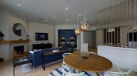 This thoughtfully designed single-floor space offers an open-plan layout that seamlessly integrates multiple functional zones into one cohesive environment. The lounge area anchors the space with a deep navy blue sofa, a sleek media console with a wall-mounted TV, and a striped area rug that adds a touch of casual sophistication. Adjacent to the lounge, a round wood dining table surrounded by light mint chairs provides an inviting spot for gathering, elegantly lit by a cluster of striking copper globe pendant lights that serve as a visual centerpiece. A built-in workstation area set against a rich navy blue accent wall offers dual computer stations, making it ideal for productivity within a shared setting. Horizontal shiplap wall paneling adds texture and a contemporary coastal feel throughout the space, while light tile flooring and recessed ceiling lighting contribute to a bright, airy ambiance. The open layout and carefully curated furnishings create a balance between comfort and functionality, making this space well-suited for both relaxation and focused work. The interplay of navy, copper, and natural wood tones lends the space a warm yet modern character.