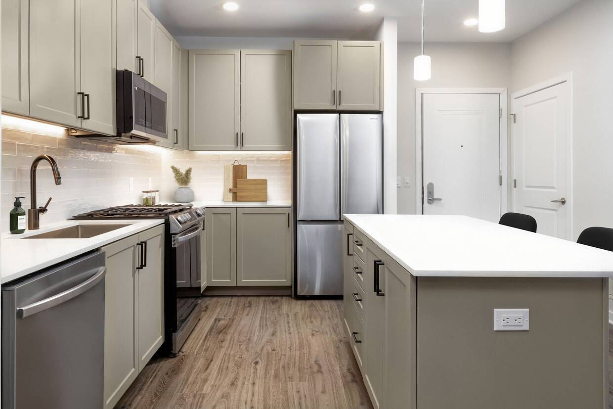 Kitchen with stainless steel appliances, quartz countertops, tile backsplash, grey cabinetry, and hard surface flooring (representative imagery) - Avalon Princeton on Harrison