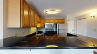 Located at 650 Bulfinch Dr in Andover, Massachusetts, this single-floor residence offers a thoughtfully designed layout with functional living spaces throughout. The kitchen is a standout feature, showcasing warm honey-toned cabinetry that extends to the ceiling for ample storage, dark granite countertops, and a full suite of stainless steel appliances including a refrigerator, range, and built-in microwave. A peninsula counter provides additional workspace and a natural transition into the main living area. The living room features rich hardwood flooring, neutral wall tones, and windows that invite natural light, complemented by baseboard heating units along the perimeter. The bedrooms are finished with plush wall-to-wall carpeting, neutral walls, and generous closet space with bifold doors. Windows in the bedrooms offer views of surrounding greenery, adding a sense of calm to each room. The bathroom is clean and well-appointed, featuring white subway tile wainscoting, a tub-shower combination, and a dark granite vanity countertop that echoes the kitchen's finishes. Textured ceilings are consistent throughout the unit, contributing to a cohesive interior aesthetic. Overall, the space presents a practical and comfortable living environment in a desirable Andover location.