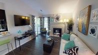 Located at 4500 E 82nd St in Indianapolis, Indiana, this single-floor residence offers a thoughtfully designed layout with a range of modern finishes throughout. The living room serves as the heart of the home, featuring vaulted ceilings, rich dark hardwood flooring, and a tiled fireplace as a central focal point. A sliding glass door floods the space with natural light and opens directly onto a private wooden balcony with outdoor views. The dining area is defined by a pendant light fixture and wainscoting detail along the walls, creating an intimate setting for meals. The kitchen features granite countertops with dark cabinetry and provides a convenient pass-through view to the dining space. An in-unit stacked washer and dryer is tucked neatly off the kitchen corridor, adding everyday practicality. The bedroom is generously sized with plush carpeting, large windows with ample natural light, and access to a walk-in closet. Two full bathrooms are appointed with dark vanity cabinetry, white countertops, large mirrors with vanity lighting, and tile shower surrounds. Throughout the residence, a neutral gray and white color palette creates a clean, cohesive aesthetic that complements both the architectural details and the overall sense of comfortable, modern living.