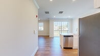 This well-appointed single-floor residence offers a thoughtfully designed open-concept layout that seamlessly connects the kitchen, dining, and living areas. The kitchen is a standout feature, showcasing white shaker-style cabinetry extending to the ceiling, a light quartz countertop island with an undermount sink, a subway tile backsplash, and a full suite of stainless steel appliances including a gas range, built-in microwave, dishwasher, and refrigerator. Recessed lighting and crown molding throughout the main living area add a refined touch, while warm hardwood flooring flows across the open living space. Large sliding glass doors lead to a private balcony, flooding the interior with generous natural light and offering outdoor views of surrounding greenery. The bedrooms are finished with plush carpeting and feature sliding closet doors with built-in shelving, providing ample storage. The bathroom is clean and functional, appointed with a white vanity, quartz countertop, and light tile flooring. The overall ambiance of the residence is fresh, modern, and bright, with a neutral palette of whites and warm beiges that creates a welcoming and versatile living environment.