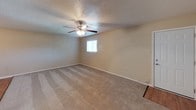 This single-story space is designed with a practical, consistent aesthetic throughout. The living area is generously sized, featuring neutral beige carpet, a textured ceiling, and a ceiling fan with an integrated light fixture. A window fitted with horizontal blinds allows natural light to filter in, creating a comfortable atmosphere. An open doorway connects the living area directly to the kitchen, promoting an easy flow between spaces.

The kitchen is well-appointed with white cabinetry above and below the counter, a double stainless steel sink, and light wood-look flooring. A white refrigerator and dishwasher are included, and a door off the kitchen provides additional access.

The bedrooms continue the carpeted flooring and neutral wall tones, each equipped with ceiling fans and ample wall space. One bedroom includes direct access to a bathroom and an adjacent closet, offering added convenience.

Two bathrooms serve the unit, both finished consistently with white vanities, arched mirrors, chrome light fixtures, and warm beige walls. One bathroom features a shower-tub combination, while the other is configured as a half bath. The overall ambiance throughout is clean, neutral, and move-in ready.