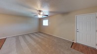 This single-story space is designed with a practical, consistent aesthetic throughout. The living area is generously sized, featuring neutral beige carpet, a textured ceiling, and a ceiling fan with an integrated light fixture. A window fitted with horizontal blinds allows natural light to filter in, creating a comfortable atmosphere. An open doorway connects the living area directly to the kitchen, promoting an easy flow between spaces.

The kitchen is well-appointed with white cabinetry above and below the counter, a double stainless steel sink, and light wood-look flooring. A white refrigerator and dishwasher are included, and a door off the kitchen provides additional access.

The bedrooms continue the carpeted flooring and neutral wall tones, each equipped with ceiling fans and ample wall space. One bedroom includes direct access to a bathroom and an adjacent closet, offering added convenience.

Two bathrooms serve the unit, both finished consistently with white vanities, arched mirrors, chrome light fixtures, and warm beige walls. One bathroom features a shower-tub combination, while the other is configured as a half bath. The overall ambiance throughout is clean, neutral, and move-in ready.