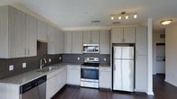 Located on Foster Street in Durham, North Carolina, this single-floor residence offers a contemporary design with thoughtful finishes throughout. The kitchen serves as a standout feature, showcasing light-toned, flat-front cabinetry with brushed metal hardware that extends floor to ceiling for generous storage. A mosaic tile backsplash adds texture and visual interest, complementing the granite-style countertops and deep undermount sink. Stainless steel appliances — including a French door refrigerator, electric range, built-in microwave, and dishwasher — lend a polished, modern aesthetic. Rich dark hardwood flooring runs throughout, providing a striking contrast against the lighter cabinetry and neutral walls. Track lighting overhead ensures the kitchen is well-lit and functional. The overall ambiance of the space is clean, modern, and move-in ready, with a design sensibility that balances practicality with contemporary style. Its location in Durham, NC places it within reach of the city's vibrant dining, arts, and cultural scene, making it an appealing option for those seeking urban convenience paired with refined interior living.