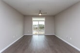This single-floor residence showcases a clean, modern design with warm neutral tones and hardwood-style flooring carried consistently throughout the space. The open-concept kitchen and living area serves as the heart of the unit, featuring dark cabinetry with a tile backsplash, stainless steel appliances including a refrigerator, dishwasher, and microwave, and a central island with a light countertop that doubles as a breakfast bar. Pendant lighting and recessed ceiling lights illuminate the space effectively.

The bedrooms are well-proportioned, each finished with the same hardwood-style flooring and neutral walls. One bedroom includes a ceiling fan and a window with blinds, while another opens directly onto a private balcony through sliding glass doors, offering outdoor views and abundant natural light. The bathroom presents a contemporary aesthetic with navy cabinetry, a light quartz countertop, an undermount sink, a large vanity mirror, and a tiled walk-in shower. White panel doors and clean white baseboards complement the overall cohesive design. The layout provides a functional, well-connected flow between all areas of the residence.