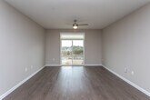 This single-floor residence showcases a clean, modern design with warm neutral tones and hardwood-style flooring carried consistently throughout the space. The open-concept kitchen and living area serves as the heart of the unit, featuring dark cabinetry with a tile backsplash, stainless steel appliances including a refrigerator, dishwasher, and microwave, and a central island with a light countertop that doubles as a breakfast bar. Pendant lighting and recessed ceiling lights illuminate the space effectively.

The bedrooms are well-proportioned, each finished with the same hardwood-style flooring and neutral walls. One bedroom includes a ceiling fan and a window with blinds, while another opens directly onto a private balcony through sliding glass doors, offering outdoor views and abundant natural light. The bathroom presents a contemporary aesthetic with navy cabinetry, a light quartz countertop, an undermount sink, a large vanity mirror, and a tiled walk-in shower. White panel doors and clean white baseboards complement the overall cohesive design. The layout provides a functional, well-connected flow between all areas of the residence.