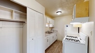 Located at 2320 Normandy Dr in Michigan City, Indiana, this single-floor unit offers a straightforward and functional layout designed for comfortable everyday living. The kitchen is efficiently arranged in a galley style, featuring white cabinetry with brushed nickel hardware, light granite-look countertops, a double stainless steel sink, and wood-look vinyl flooring. White appliances, including a refrigerator and gas range, are included, and a louvered bi-fold closet door provides convenient in-kitchen storage. Upper and lower cabinets offer ample space for pantry and cookware storage. The living area is generously sized, with neutral-toned carpet underfoot and a wall-mounted air conditioning unit providing climate control. The open wall space allows for flexible furniture arrangement. The bedrooms are carpeted and finished with the same warm, neutral palette. Each room benefits from natural light through windows fitted with horizontal blinds, offering views of the surrounding residential neighborhood. Textured ceilings are present throughout the unit, contributing to its consistent, understated aesthetic. The overall layout, as shown in the floor plan scan, includes a bathroom and defined entry area, creating a cohesive and practical living environment.