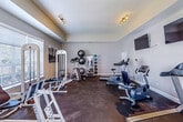 This fitness center in Robinsonville, Mississippi, offers a thoughtfully organized single-floor layout designed to support a well-rounded workout routine. The space features neutral gray walls, dark flooring, and elevated ceilings with tray ceiling detail in one section, contributing to an open and airy atmosphere. Track lighting throughout provides consistent illumination, while windows fitted with blinds allow natural light to filter in.

The cardio zone is equipped with treadmills, an upright stationary bike, and a recumbent bike, all positioned facing two wall-mounted flat-screen televisions for an engaging workout experience. Strength training is supported by a multi-use cable machine, weight benches, and a leg press/sled apparatus. A dedicated accessories station holds an organized rack of medicine balls in varying weights alongside stability balls of multiple sizes, resistance bands, and jump ropes, offering options for functional and flexibility training.

French doors provide access to the space, enhancing the welcoming feel of the facility. The dark rubber-style flooring is durable and practical for the range of equipment and activities accommodated. Overall, the fitness center presents a clean, functional environment suitable for a variety of fitness levels and training styles.