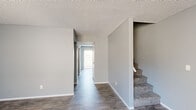 This two-story home offers a well-organized layout across two floors, providing 3 bedrooms and 3 bathrooms. The main floor features a living room and kitchen connected by hallways with durable wood-look flooring throughout. The kitchen is equipped with white cabinetry, speckled countertops, a coil-top electric range, and a refrigerator, all arranged in an efficient galley-style configuration. A bathroom on the main level includes a white vanity with a speckled countertop, a framed mirror with overhead lighting, and wood-look flooring. The staircase, carpeted for comfort, leads to the upper floor where the three bedrooms are located. Each bedroom features soft carpeting, neutral gray walls, and textured ceilings. The bedrooms are well-proportioned, with the primary bedroom offering a comfortable footprint. Bedrooms include sliding-door closets for storage. Additional bathrooms on the upper level mirror the clean, functional design of the main-floor bathroom. Throughout the home, a consistent neutral gray color palette, white trim, and textured ceilings create a cohesive and clean aesthetic. Natural light filters in through windows fitted with vertical blinds, contributing to a bright and livable atmosphere across both levels.