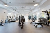 Located at 25 Silver Moon Circle in St. Augustine, FL, this fitness center offers a comprehensive, single-floor layout spanning a generously sized footprint designed to accommodate a wide range of workout needs. The facility is divided into distinct zones, each purpose-built for specific training disciplines.

The main gym floor features an extensive selection of Matrix strength machines, free weights, benches, and a full dumbbell rack, alongside cardio equipment including treadmills, ellipticals, stair climbers, and rowing machines. The space is finished with durable rubber flooring and light hardwood in the cardio area, complemented by coffered ceilings, large ceiling fans, and pendant lighting that create a bright, airy atmosphere. Arched windows throughout allow abundant natural light to fill the space.

A dedicated cycling studio accommodates multiple stationary bikes arranged in rows, finished with plush carpet flooring, a tray ceiling with warm ambient uplighting, wall-mounted sconces, and expansive arched windows overlooking the outdoors — creating an energizing yet refined environment.

A separate multipurpose studio provides an open, flexible space ideal for group fitness, yoga, or functional training, outfitted with carpeted flooring, a tray ceiling, natural light from multiple arched windows, and wall-mounted accessories. The overall design balances a clean, upscale aesthetic with practical, high-performance fitness functionality.