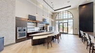 Located at 211 River Landing Dr in Charleston, SC, this generously sized single-floor community space offers a sophisticated and welcoming environment designed for both relaxation and social gatherings. The open layout is unified by elegant herringbone-patterned light wood flooring that flows seamlessly throughout.

The kitchen and bar area is a standout feature, showcasing a curved, oversized island with a white countertop, dark cabinetry, a tiled backsplash, and pendant globe lighting. A dramatic arched window with a gridded frame floods the space with natural light and offers views of the surrounding exterior. Double glass doors open directly to an outdoor area.

The living room is anchored by a striking white stone accent wall hosting a wall-mounted flat-screen TV and a floating media console. Soaring tray ceilings with clerestory windows draw in additional natural light, while soft blue sofas, accent chairs, and coastal-inspired artwork contribute to a calm, refined ambiance.

Adjacent to the living area, a billiards room provides a dedicated recreation zone, complete with a full-size pool table, a textured wall panel, a mounted TV, and cue storage. Throughout the space, dark wood columns create visual definition between zones. The overall design balances contemporary elegance with comfort, making it an ideal gathering space.
