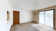 This 2-bedroom, 1-bathroom residence is thoughtfully laid out across a single floor, offering a straightforward and functional living environment. The living area features neutral-toned carpeting that adds warmth underfoot, along with clean white walls that create a bright, open feel. A sliding glass door floods the space with natural light and provides convenient access to the outdoors, while vertical blinds offer privacy and light control. Climate comfort is well-addressed, with both a wall-mounted air conditioning unit and a baseboard heating system ensuring year-round temperature regulation. The entry door is finished in warm wood tones, complementing the room's understated aesthetic. The overall design is clean and minimal, prioritizing practicality and ease of living. The two bedrooms offer comfortable personal retreats, while the single bathroom serves the household with efficient use of space. The layout is well-suited for individuals, couples, or small families seeking a manageable, single-level living arrangement with essential amenities in place.