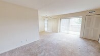 Located at 2107 Prior Rd in Wilmington, Delaware, this one-bedroom, one-bathroom apartment offers a well-organized, single-floor layout designed for comfortable everyday living. The living area is generously proportioned, featuring plush wall-to-wall carpeting in warm neutral tones and a large sliding glass door fitted with vertical blinds that floods the space with natural light while providing access to the outdoors. A chandelier adds a touch of elegance to the open living and dining area. The bedroom is comfortably sized, also carpeted, and includes a walk-in closet with built-in shelving for ample storage. Additional closet space is visible throughout the unit, including double closet doors in the main living area. The bathroom is cleanly appointed with tile flooring, a single-vanity with under-sink cabinetry, a full soaking tub and shower combination, and a decorative oval mirror above the sink beneath a classic vanity light fixture. Neutral beige walls and light-toned finishes carry throughout the unit, creating a cohesive and bright ambiance. A hallway connects the main living spaces to the bedroom and bathroom, and the entrance provides a practical transition into the home. The layout makes efficient use of its footprint, offering a comfortable and functional living environment.