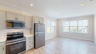 Located at 164 Blossom St in Lynn, Massachusetts, this thoughtfully designed single-floor residence offers a clean, contemporary aesthetic throughout. Light hardwood flooring flows continuously across every room, complemented by neutral warm-gray walls, crisp white trim, and crown molding that adds a refined architectural touch.

The kitchen is a standout feature, equipped with full-height gray shaker-style cabinetry, black hardware accents, white quartz countertops, and a complete suite of stainless steel appliances including a refrigerator, range, over-the-range microwave, and dishwasher. Recessed lighting and proximity to large windows keep the kitchen bright and open to an adjoining living or dining area.

The bedrooms are generously proportioned, each benefiting from large windows that frame views of the surrounding neighborhood and allow abundant natural light to fill the space. Crown molding and recessed ceiling details are consistent throughout. One bedroom features a convenient en-suite bathroom, adding a layer of privacy.

The bathroom is finished with light tile flooring, a gray vanity with a white countertop and under-mount sink, a well-lit mirror with a brushed nickel vanity light, and a full tub-shower combination. Additional louvered closet doors and ample storage are visible throughout the unit, rounding out a practical and polished living environment.