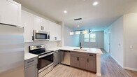 Located at Integra Town Center in Daytona Beach, FL, this well-appointed one-bedroom, one-bathroom residence offers a thoughtfully designed single-floor layout. The open-concept kitchen serves as the heart of the home, showcasing two-tone cabinetry with crisp white upper cabinets and warm gray lower cabinets, quartz countertops, stainless steel appliances, and a peninsula island with an undermount sink and matte black faucet. A trio of pendant lights illuminates the island, creating a stylish focal point that flows seamlessly into the living area. Durable wood-look plank flooring extends throughout the entire space, adding warmth and continuity. The living area is bright and airy, benefiting from natural light admitted through windows and complemented by a ceiling fan. The primary bedroom is a comfortable retreat with dual windows, a ceiling fan, and a dedicated closet for storage. The bathroom is finished in a modern aesthetic, featuring a dark-framed glass-enclosed shower, a sleek vanity with a white countertop, a large mirror, and matte black hardware accents. Clean neutral walls and recessed lighting throughout the home create a fresh, contemporary ambiance ideal for comfortable living.