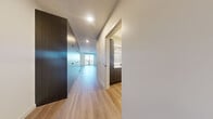 This contemporary one-bedroom, one-bathroom residence at 21 Boston St in Seattle's Queen Anne neighborhood offers a thoughtfully designed open-concept layout finished with light hardwood-style flooring throughout. The living area is bathed in natural light from large floor-to-ceiling windows and sliding glass doors that open onto a private balcony overlooking the surrounding neighborhood skyline.

The kitchen is well-appointed with two-tone cabinetry — pairing light wood uppers with darker lower cabinets — a classic white subway tile backsplash, white quartz countertops, and a full suite of black appliances including a refrigerator, range, dishwasher, and microwave. A substantial floor-to-ceiling dark wood storage unit in the living area provides abundant built-in storage and adds a bold design element to the space.

The bedroom is a calm, light-filled retreat with sliding glass door access to the balcony and an additional tall window that frames views of the city. The hallway features a dedicated closet for additional storage.

The bathroom is sleekly modern, featuring dark wood cabinetry, a white quartz vanity, black fixtures, and a subway-tiled shower-tub combination. A stacked in-unit washer and dryer is conveniently integrated into the bathroom, adding practical everyday functionality to this well-designed Seattle residence.