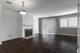 This two-story residence in Los Angeles (90066) offers a well-organized layout across two distinct levels connected by a carpeted staircase with a white baluster railing. The main level features rich hardwood flooring throughout the living and dining areas, anchored by a tiled fireplace with a clean white mantle. A sliding glass door and adjacent window flood the living space with natural light and provide outdoor views, complemented by vertical blinds for privacy. The kitchen is outfitted with dark granite countertops, rich cherry wood cabinetry, a mosaic tile backsplash, and stainless steel appliances including a refrigerator, electric range, and over-the-range microwave. Tile flooring transitions seamlessly from the kitchen toward the entryway. Upstairs, the bedrooms are finished with plush carpeting and feature windows with natural light. One bedroom includes an en-suite bathroom with a glass-enclosed shower and tiled flooring. A shared bathroom on the upper level showcases dark granite countertops, a cherry wood vanity, dual mirrors, and a chandelier-style light fixture, echoing the refined finishes found throughout the home.