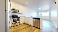This well-appointed single-floor unit offers a thoughtfully designed layout with a clean, contemporary aesthetic throughout. The kitchen serves as a functional centerpiece, featuring white shaker-style cabinetry, granite-look countertops, and a full suite of stainless steel appliances including a refrigerator, electric range, over-the-range microwave, and dishwasher. A peninsula provides additional counter space and creates a natural transition into the open living area, which is bathed in natural light from large windows. Light-toned wood-look flooring extends throughout the main living spaces, lending warmth and visual continuity. The bedrooms offer plush neutral carpeting and ample wall space, with one room featuring a window that frames an outdoor view and access to natural light. Closet space is included for added practicality. The bathroom is finished with wood-look vinyl flooring, white cabinetry, and a clean, minimal design. A standout feature of this unit is the generously sized private balcony, enclosed by a metal railing and offering expansive open-sky views — an ideal outdoor retreat. Recessed lighting and crisp white walls throughout contribute to a bright, airy ambiance that defines the overall character of this space.