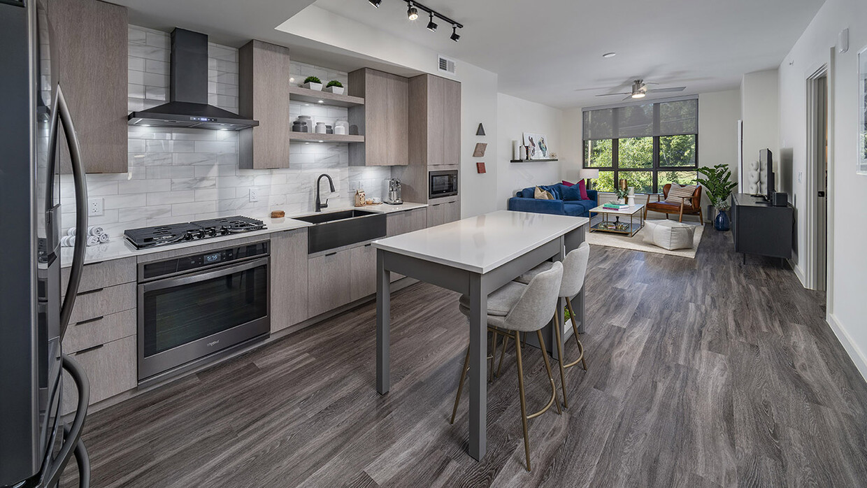 Apartment kitchen with stainless steel appliances, dining and living room with wood-style flooring. - Griffis Edgemoor