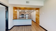 Located at 3212 Jaffa Garden Way in Rapid City, South Dakota, this single-floor residence offers a thoughtfully designed layout with modern finishes and functional living spaces. The kitchen serves as a visual centerpiece, framed by striking warm-toned wood accent walls that extend from floor to ceiling on either side, creating a bold architectural statement. A peninsula with dark stone countertops provides an ideal space for casual dining or food prep, while pendant lighting adds a refined touch overhead. Stainless steel appliances, including a refrigerator, range, and microwave, complement the light wood cabinetry for a clean, contemporary aesthetic. Durable light wood-tone flooring flows throughout the space, tying each area together cohesively. The bedroom is a calm, neutral retreat featuring a ceiling fan, baseboard heating, and a window that brings in natural light and views of surrounding greenery. The bathroom is finished with a clean walk-in shower featuring white shiplap-style surround walls, built-in corner shelves, and brushed nickel fixtures. A dedicated utility area accommodates an in-unit washer, adding everyday convenience. Overall, the space presents a well-appointed, move-in-ready living environment with modern design sensibilities.