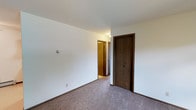 This single-floor, 2-bedroom, 1-bathroom unit offers a practical and comfortable layout designed for everyday living. The interior is finished with neutral, light-colored walls and wall-to-wall carpeting throughout the main living areas and bedrooms, creating a warm and cohesive feel.

The living area is generously sized, featuring a large picture window that frames outdoor views and floods the room with natural light. A baseboard heating system runs along the perimeter, ensuring consistent warmth. The space flows openly, providing ample room for a variety of furniture arrangements.

Both bedrooms are well-proportioned and carpeted, each featuring dark wood-trimmed closet doors. The primary bedroom benefits from two windows and a ceiling fan with integrated lighting, while the second bedroom also includes a ceiling fan, a large window, and baseboard heating.

The kitchen is efficiently laid out in a U-shaped configuration, outfitted with rich dark wood cabinetry, a double-basin sink, and white appliances including a refrigerator and electric range with hood ventilation. The flooring transitions to a smooth, easy-to-clean surface in this area.

The full bathroom includes a single-sink vanity with dark wood cabinetry, a framed mirror with wall-mounted lighting, a toilet, and a full tub-shower combination with a curtain rod — all finished in neutral, easy-to-maintain tones.