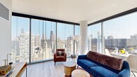 Located at 300 N Michigan Avenue in the heart of Chicago, this high-rise residence offers a stunning blend of contemporary design and breathtaking urban panoramas. The living area is defined by wraparound floor-to-ceiling glass windows that frame sweeping views of the Chicago skyline, including iconic landmarks and the Chicago River below, flooding the space with abundant natural light. Light-toned hardwood flooring runs throughout, complementing the clean, modern aesthetic. The galley-style kitchen is outfitted with sleek white cabinetry, stainless steel appliances including a gas range and French door refrigerator, and light countertops, with city views visible even from the kitchen window. A private balcony extends the living space outdoors, offering direct open-air access to the skyline. The bedrooms continue the floor-to-ceiling window design, ensuring every room benefits from the spectacular views and natural light. Bathrooms are finished in a crisp, minimalist style featuring large-format tile flooring, white vanities with black hardware accents, framed mirrors, and glass-enclosed showers. A bright, well-proportioned hallway connects the rooms, completing this thoughtfully designed urban residence.