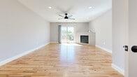 This three-floor home offers a well-organized layout across three distinct levels, accommodating three bedrooms and three full bathrooms. The ground floor serves as the entry point, featuring a welcoming entrance, a living room, and a spacious combined kitchen and living area. The kitchen is a standout feature, showcasing slate-blue shaker-style cabinetry, white subway tile backsplash, stainless steel appliances, a peninsula with pendant lighting, and warm hardwood flooring that flows throughout the main living areas. The main floor is the most expansive level, housing two living areas, hallways, and additional staircases, with hardwood floors and ceiling fans lending a bright, airy feel. A sliding glass door in one living area opens to an outdoor view of green surroundings, filling the space with natural light. The upper floor contains the bedrooms, including a generously sized primary bedroom with plush carpeting, a ceiling fan, and a large window. Bedrooms include closets with built-in shelving. The three bathrooms are finished with clean, neutral palettes—one featuring tile flooring with a tub-shower combo, another with wood-look vinyl flooring and a gray vanity with matte black hardware. Throughout, the home maintains a cohesive, modern aesthetic with soft gray walls and crisp white trim.