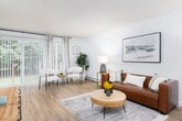 This single-story unit offers a thoughtfully arranged layout with distinct living, dining, kitchen, and sleeping areas. The living room features light wood-style flooring, neutral white walls, a textured ceiling, and baseboard heating. A sliding glass door and vertical blinds in the dining area invite natural light and provide outdoor views, complemented by a pendant light fixture above the dining table and a circular mirror accent on the wall.

The kitchen is efficiently designed with dark wood cabinetry, light countertops, and a full suite of stainless steel appliances, including a refrigerator, electric range, and over-the-range microwave. A flush-mount ceiling light and electrical panel are conveniently positioned near the kitchen entry.

A separate sitting or flex room adjacent to the living area offers additional natural light through large windows dressed with layered curtains and vertical blinds, along with its own baseboard heating unit.

The bedroom is carpeted for comfort, featuring a generously sized closet with louvered sliding doors, a natural light-admitting window with blinds, and a textured ceiling. The space maintains a clean, neutral palette throughout, creating a cohesive and functional environment.