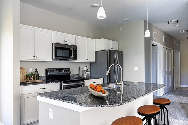 Modern kitchen with sleek granite countertops and stainless steel appliances under elegant pendant lighting. - Aspen Lakes