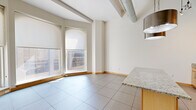 Located at 225 N Eighth St in the heart of downtown St. Louis, this one-bedroom, one-bathroom urban loft blends industrial character with modern comfort. The open-concept living and dining area makes a bold first impression with soaring ceilings, exposed spiral ductwork, and large format tile flooring that runs throughout the main living space. A curved bay of floor-to-ceiling windows floods the room with natural light while framing dynamic views of the surrounding cityscape.

The kitchen is a functional centerpiece, featuring light maple cabinetry, granite countertops, a glass tile backsplash, stainless steel appliances including a range, microwave, and refrigerator, and a peninsula island with pendant lighting overhead — ideal for both cooking and casual dining.

The bedroom offers a quieter retreat, carpeted for comfort and equipped with two generous closets fitted with wire shelving, providing ample storage. The full bathroom is clean and well-appointed, with large-format tile flooring, a soaking tub with shower, a wood-framed vanity, and a neutral palette that complements the rest of the home.

A connecting hallway ties the layout together efficiently. This loft-style residence delivers a distinctly urban living experience in the vibrant core of St. Louis.