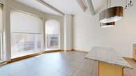 Located at 225 N Eighth St in the heart of downtown St. Louis, this one-bedroom, one-bathroom urban loft blends industrial character with modern comfort. The open-concept living and dining area makes a bold first impression with soaring ceilings, exposed spiral ductwork, and large format tile flooring that runs throughout the main living space. A curved bay of floor-to-ceiling windows floods the room with natural light while framing dynamic views of the surrounding cityscape.

The kitchen is a functional centerpiece, featuring light maple cabinetry, granite countertops, a glass tile backsplash, stainless steel appliances including a range, microwave, and refrigerator, and a peninsula island with pendant lighting overhead — ideal for both cooking and casual dining.

The bedroom offers a quieter retreat, carpeted for comfort and equipped with two generous closets fitted with wire shelving, providing ample storage. The full bathroom is clean and well-appointed, with large-format tile flooring, a soaking tub with shower, a wood-framed vanity, and a neutral palette that complements the rest of the home.

A connecting hallway ties the layout together efficiently. This loft-style residence delivers a distinctly urban living experience in the vibrant core of St. Louis.