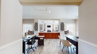 Located on Ligon Mill Road in Wake Forest, NC, this single-story community clubhouse is designed to impress with a thoughtful blend of elegance and functionality. The centerpiece of the space is a grand lounge area showcasing soaring vaulted ceilings with a dramatic floor-to-ceiling window wall that floods the room with natural light. A classic white fireplace anchors one end of the lounge, which is furnished with comfortable seating and complemented by wood-look tile flooring that flows seamlessly throughout the entire facility.

The reception area features a wide granite-topped counter with pendant lighting and rich cherry wood cabinetry, creating a polished and welcoming first impression. Adjacent private offices are well-appointed, each with large windows adorned with deep navy drapes, ample workspace, and direct views of the surrounding outdoor areas.

A fully equipped kitchen offers stainless steel appliances, granite countertops, rich cherry cabinetry, and a double sink — ideal for hosting community events. A dedicated beverage station provides added convenience for residents and guests.

Wainscoting panels, crown molding, and decorative column details lend an upscale, refined character to the space, while abundant windows ensure a bright and inviting atmosphere throughout.
