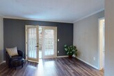 This single-floor residence offers a well-designed layout that balances comfort and modern style throughout its living spaces. The open living area is a standout, featuring rich, dark wood-look flooring that extends seamlessly through the main areas. Crown molding lines the ceilings, adding a refined architectural detail, while a bold navy accent wall creates a striking focal point. Natural light pours in through a set of French doors fitted with plantation shutters, providing both brightness and a direct connection to the outdoor patio beyond.

The kitchen has been thoughtfully updated with crisp white cabinetry accented by matte black hardware, a classic white subway tile backsplash, and dark quartz-style countertops. A stainless steel sink with a contemporary faucet and stainless steel appliances complete the functional and attractive space.

The bedroom offers plush carpeting, crown molding, a ceiling fan with a light fixture, and a window with blinds that allow for natural light and privacy. A hallway connects the bedroom to the bathroom, which features wood-look flooring and clean, neutral finishes.

Throughout the unit, a neutral color palette, consistent trim work, and quality flooring choices come together to create a cohesive, inviting atmosphere.