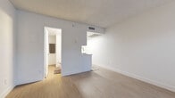 This thoughtfully designed studio unit makes smart use of its compact footprint, offering a single-floor layout that combines a kitchen and living area with one full bathroom. The open living space is finished with light wood-style plank flooring and neutral white walls, creating a clean, airy aesthetic throughout. A large window fitted with blinds allows natural light to fill the room, contributing to a bright and welcoming ambiance. A textured ceiling adds a subtle architectural element overhead.

The kitchen is efficiently laid out in a galley configuration, featuring white shaker-style cabinetry with brushed nickel hardware, a white quartz countertop, and a classic white subway tile backsplash. Stainless steel appliances — including a refrigerator, range, and over-the-range microwave — provide a modern, functional cooking space. A peninsula counter with a single-basin sink bridges the kitchen to the living area with an open pass-through design.

The bathroom is finished with consistent white cabinetry, quartz countertops, and brushed nickel fixtures, including a single undermount sink with a modern faucet and a large mirror above. The cohesive design palette carries through from room to room, giving the entire unit a polished, uniform character. A front entry door with an adjacent window completes the layout.