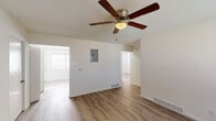 This single-floor residence offers a thoughtfully laid-out interior finished with light wood-style flooring that runs consistently throughout the home, creating a cohesive and welcoming atmosphere. The living area is spacious and open, featuring a ceiling fan with a built-in light fixture, neutral white walls, and convenient access to adjacent rooms. A dedicated electrical panel is integrated into the living space wall, and floor vents ensure efficient climate control throughout.

The kitchen is well-appointed with rich, dark espresso-toned shaker-style cabinetry that extends to the ceiling for generous storage capacity. White countertops provide a clean contrast, while appliances include a stainless steel refrigerator, a black electric range, and an over-the-range microwave. A window with blinds brings in natural light, making the kitchen feel bright and functional.

The bedrooms are generously sized, each equipped with ceiling fans, multiple windows fitted with horizontal blinds, and the same warm wood-style flooring found throughout the home. The rooms offer a bright, airy feel with ample wall space for flexible furniture arrangements.

The bathroom is clean and efficiently designed, featuring a full tub and shower combination with built-in shelving, a large mirror, and a white vanity sink, all presented in a bright, all-white finish.