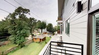 This single-floor residence is part of a contemporary multi-story building clad in light gray horizontal siding, giving it a clean, modern aesthetic. The exterior design incorporates large windows that allow natural light to filter into the living spaces, while the building's updated architectural lines reflect a current, urban sensibility.

A standout feature of this unit is its private balcony, enclosed by sleek black metal railings. The outdoor space offers open views of the surrounding neighborhood, including lush, mature trees, green lawns, and nearby residential structures — providing a pleasant natural backdrop amid an urban setting. Additional balconies are visible along the building's facade, indicating a consistent design language throughout the property.

The building's positioning elevates the unit above street level, enhancing both privacy and the quality of the outdoor views. The balcony provides a functional outdoor retreat suitable for seating or relaxing while taking in the tree-lined surroundings. The overall character of the space combines modern construction with a connection to the established neighborhood context around it.