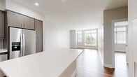 This A1B floor plan at Currents on the Charles in Waltham, MA, offers 620 square feet of modern, single-level living across two bedrooms and one bathroom. Light wood-tone flooring flows consistently throughout the unit, complementing a clean, neutral color palette that creates a bright and cohesive aesthetic.

The open-concept kitchen and living area serves as the heart of the apartment. The kitchen features taupe wood cabinetry, white quartz countertops, a subway tile backsplash, and stainless steel appliances including an electric range and over-the-range microwave. The adjacent living area benefits from large windows that invite abundant natural light and outdoor views. Recessed lighting adds to the bright, airy atmosphere.

The primary bedroom measures 120 square feet and includes a window with blinds and a dedicated closet with built-in shelving. The second bedroom mirrors the same wood flooring and neutral walls. The full bathroom is finished with large-format floor tiles, a tub-shower combination accented by vertically stacked brown wall tiles, a wood-tone vanity with a white countertop, and a framed mirror. Additional features include a walk-in closet with wire shelving, a smart thermostat, and a keypad entry door lock.