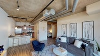 Located at 2200 Market St in Denver's vibrant Five Points neighborhood, this urban loft-style unit masterfully blends industrial aesthetics with modern comfort. The open-concept layout seamlessly connects the living, dining, and kitchen areas, all anchored by striking exposed concrete ceilings and prominent silver ductwork that define the industrial character of the space. Wide-plank hardwood flooring flows throughout, adding warmth to the raw architectural elements.

The living area is generously sized, bathed in natural light from large glass doors that open onto a private balcony, offering views of the surrounding cityscape. The kitchen features warm wood cabinetry, granite countertops, and a full suite of stainless steel appliances including a refrigerator, electric range, and built-in microwave, along with a convenient wine rack above the cabinetry.

The bedroom is a standout feature, enclosed by a sliding door and highlighted by a dramatic full-height exposed concrete accent wall that lends a bold, loft-authentic feel. The bathroom is well-appointed with a soaking tub and shower combination, tile accents, a wood vanity with granite countertop, and a large mirror. This unit offers a compelling blend of industrial design and urban convenience in the heart of Denver.