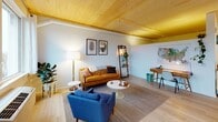 This single-floor residence showcases a cohesive mid-century modern aesthetic with warm, natural wood plank ceilings that run throughout the main living areas, creating an inviting and architecturally distinctive atmosphere. Light hardwood flooring complements the pale gray walls, lending the space a clean, airy quality.

The open-concept living area is generously proportioned, featuring a tufted caramel leather sofa, a bold blue accent chair, and a round white coffee table arranged atop a textured area rug. Botanical wall art and a lean ladder shelf add character, while a large window frames views of mature trees and the surrounding neighborhood, filling the room with natural light. A dedicated workspace is also integrated into this area.

The dining area is anchored by a rich walnut-toned table with mid-century chairs and a striking black pendant light overhead. A floor-to-ceiling window with balcony access introduces additional natural light and outdoor views, enhancing the sense of openness.

The kitchen is efficiently designed with light maple cabinetry, a white tile backsplash, under-cabinet lighting, and stainless steel appliances including a range and dishwasher, offering a functional and stylish cooking environment.

The bathroom is clean and spacious, finished with light hardwood flooring, a floating wood vanity, and a walk-in shower, maintaining the residence's consistent modern and minimalist design language throughout.