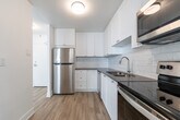 This 2-bedroom, 1-bathroom unit at 2757 Kipling Ave in Toronto's northwest end offers a clean, modern interior across a well-organized single floor. Light-toned hardwood-style flooring runs throughout, creating a bright and cohesive feel. The open living room is a standout feature, anchored by a wide floor-to-ceiling window that fills the space with natural light and frames views of the surrounding Toronto skyline. A baseboard heating unit runs beneath the windows, ensuring year-round comfort. The kitchen is thoughtfully updated with white shaker-style cabinetry, a subway tile backsplash, grey countertops, and stainless steel appliances including a refrigerator, dishwasher, range, and over-the-range microwave. The primary bedroom is generously sized, with a window for natural light and a dedicated closet. The second bedroom also features a window and easy access to the main hallway. A walk-in closet with a full-length hanging rod provides additional storage. The bathroom is finished with floor-to-ceiling white subway tile surrounding a soaker tub and shower combo with chrome fixtures. White walls and textured ceilings throughout contribute to the unit's clean, refreshed aesthetic.