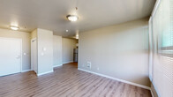 Located at 406 West Main Street in downtown Medford, Oregon, this one-bedroom, one-bathroom unit offers a practical and efficiently designed single-floor layout. Light wood-style flooring runs consistently throughout the space, lending a clean, cohesive aesthetic to every room.

The living area is the largest space in the unit, benefiting from multiple windows that allow generous natural light to fill the room. A bank of windows provides views of the surrounding Medford streetscape, enhancing the sense of openness. The kitchen is positioned adjacent to the living area and features white cabinetry, a stainless steel stove with microwave above, and a dishwasher, offering functional amenities within a compact footprint.

The bedroom is a comfortable, well-proportioned room with a closet and a window overlooking the outdoors, allowing for continued natural light. Neutral taupe-toned walls throughout the unit provide a versatile backdrop. The bathroom is outfitted with a white vanity with storage drawers, a tub-shower combination with grab bars and a curved curtain rod, and matching wood-style flooring, presenting a clean and practical space.

Overall, the unit presents a straightforward, modern interior design with consistent finishes, making efficient use of its footprint in a convenient downtown Medford location.