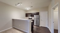 Located at 40 Hutchinson Ave in Columbus, Ohio, this single-floor residence offers a well-designed layout with modern finishes throughout. The kitchen is a standout feature, equipped with dark espresso cabinetry, light granite-style countertops, a subway tile backsplash, and a full suite of stainless steel appliances including a refrigerator, electric range, microwave, and dishwasher. A peninsula with a breakfast bar creates an open connection to the adjacent living area, which is generously proportioned and finished with durable wood-look flooring. The living room opens directly to a private balcony through a sliding glass door, allowing natural light to fill the space. Bedrooms are carpeted for comfort and offer ample room for furnishings, with neutral-toned walls providing a clean, versatile backdrop. The primary bedroom includes access to a spacious walk-in closet outfitted with wire shelving and hanging rods for organized storage. The primary bathroom features a dark vanity with a marble-style countertop, a large mirror with overhead lighting, wood-look flooring, and a walk-in shower with sliding glass doors. A second bathroom provides similar finishes with a vanity and mirror. The overall aesthetic is cohesive and contemporary, with neutral tones and quality materials used consistently throughout.