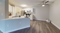 This single-floor residence is thoughtfully designed with a clean, modern aesthetic and a cohesive neutral color palette throughout. The open-concept layout connects the kitchen and living area seamlessly, creating a spacious and functional flow. The kitchen is a standout feature, equipped with white shaker-style cabinetry, white quartz countertops, stainless steel appliances including a refrigerator and electric range, a tile backsplash, and a peninsula with a sink that doubles as a breakfast bar. Hardwood-style luxury vinyl plank flooring runs throughout the main living areas, adding warmth and durability. The living area is bright and open, anchored by a ceiling fan and enhanced by a full-width sliding glass door fitted with vertical blinds, offering views of the surrounding green landscape and allowing ample natural light to fill the space. The bedroom features plush carpeting, neutral wall tones, and a window with exterior views, creating a comfortable and restful retreat. The bathroom is well-finished with wood-look vinyl flooring, a full tub-shower combination, a white vanity with a clean countertop, and brushed nickel fixtures. A dedicated laundry area with washer and dryer hookups adds practical convenience to this move-in-ready residence.
