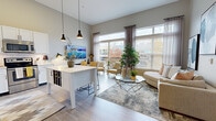 Located at 7569 Gibson St in Liberty Township, Ohio, this thoughtfully designed one-bedroom, one-bathroom residence offers a cohesive open-concept floor plan across a single level. The combined kitchen and living area serves as the heart of the home, showcasing soaring ceilings, light wood-look flooring, and oversized windows with balcony access that flood the space with natural light and outdoor views. The modern kitchen features crisp white cabinetry, subway tile backsplash, stainless steel appliances, and a white island with bar seating, all beneath stylish pendant lighting. The living area flows seamlessly from the kitchen, offering generous room for lounging and entertaining. The primary bedroom is a bright, comfortable retreat with large windows, plush carpeting, and ample space. The full bathroom impresses with a dual-sink vanity, white shaker cabinetry, and a tiled tub-shower combination. A dedicated office provides a quiet, carpeted space with built-in wall shelving, ideal for working from home. A closet completes the layout, providing practical storage. Neutral tones, contemporary fixtures, and abundant natural light give the entire residence a clean, modern ambiance.