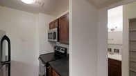 This single-floor space is designed with functionality and practicality in mind. The kitchen serves as a central feature, showcasing rich, dark-stained wood cabinetry that provides ample storage both above and below the countertops. The dark countertops complement the cabinetry, creating a cohesive and grounded aesthetic throughout the cooking area. Stainless steel appliances, including an electric range and an over-the-range microwave, lend a modern touch to the kitchen and enhance its overall utility. The layout makes efficient use of the available space, with the appliances thoughtfully positioned for ease of use. A ceiling vent indicates a climate-controlled environment, ensuring year-round comfort. The clean white walls throughout create a bright, neutral backdrop that contrasts nicely with the darker tones of the kitchen fixtures. The overall ambiance of the space is clean, understated, and move-in ready, making it well-suited for those who value a straightforward, no-frills living environment with all the essential amenities in place.