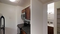 This single-floor space is designed with functionality and practicality in mind. The kitchen serves as a central feature, showcasing rich, dark-stained wood cabinetry that provides ample storage both above and below the countertops. The dark countertops complement the cabinetry, creating a cohesive and grounded aesthetic throughout the cooking area. Stainless steel appliances, including an electric range and an over-the-range microwave, lend a modern touch to the kitchen and enhance its overall utility. The layout makes efficient use of the available space, with the appliances thoughtfully positioned for ease of use. A ceiling vent indicates a climate-controlled environment, ensuring year-round comfort. The clean white walls throughout create a bright, neutral backdrop that contrasts nicely with the darker tones of the kitchen fixtures. The overall ambiance of the space is clean, understated, and move-in ready, making it well-suited for those who value a straightforward, no-frills living environment with all the essential amenities in place.