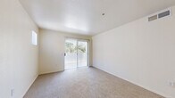 This single-floor residence offers a practical and comfortable layout encompassing a bedroom, bathroom, kitchen, living room, and hallway. The open living area features neutral-toned carpet flooring, light-colored walls, and a sliding glass door that floods the space with natural light and provides access to an outdoor area with greenery views. The kitchen is efficiently designed with light wood cabinetry, tile flooring, and a full suite of appliances including a range, refrigerator, microwave, and dishwasher. A breakfast bar-style counter connects the kitchen to the living space, creating a cohesive, open flow between the two areas. The generously sized primary bedroom is carpeted and bright, featuring a ceiling fan with light fixture, a large window with vertical blinds offering natural light and outdoor views, and ample wall space for furnishings. The full bathroom is finished with tile flooring, a tub-shower combination with tiled surround, a toilet, and a vanity with light wood cabinetry, a wide countertop, and a large mirror. Neutral tones and clean finishes throughout give the space a bright, functional, and move-in-ready character.