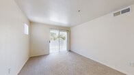 This single-floor residence offers a practical and comfortable layout encompassing a bedroom, bathroom, kitchen, living room, and hallway. The open living area features neutral-toned carpet flooring, light-colored walls, and a sliding glass door that floods the space with natural light and provides access to an outdoor area with greenery views. The kitchen is efficiently designed with light wood cabinetry, tile flooring, and a full suite of appliances including a range, refrigerator, microwave, and dishwasher. A breakfast bar-style counter connects the kitchen to the living space, creating a cohesive, open flow between the two areas. The generously sized primary bedroom is carpeted and bright, featuring a ceiling fan with light fixture, a large window with vertical blinds offering natural light and outdoor views, and ample wall space for furnishings. The full bathroom is finished with tile flooring, a tub-shower combination with tiled surround, a toilet, and a vanity with light wood cabinetry, a wide countertop, and a large mirror. Neutral tones and clean finishes throughout give the space a bright, functional, and move-in-ready character.